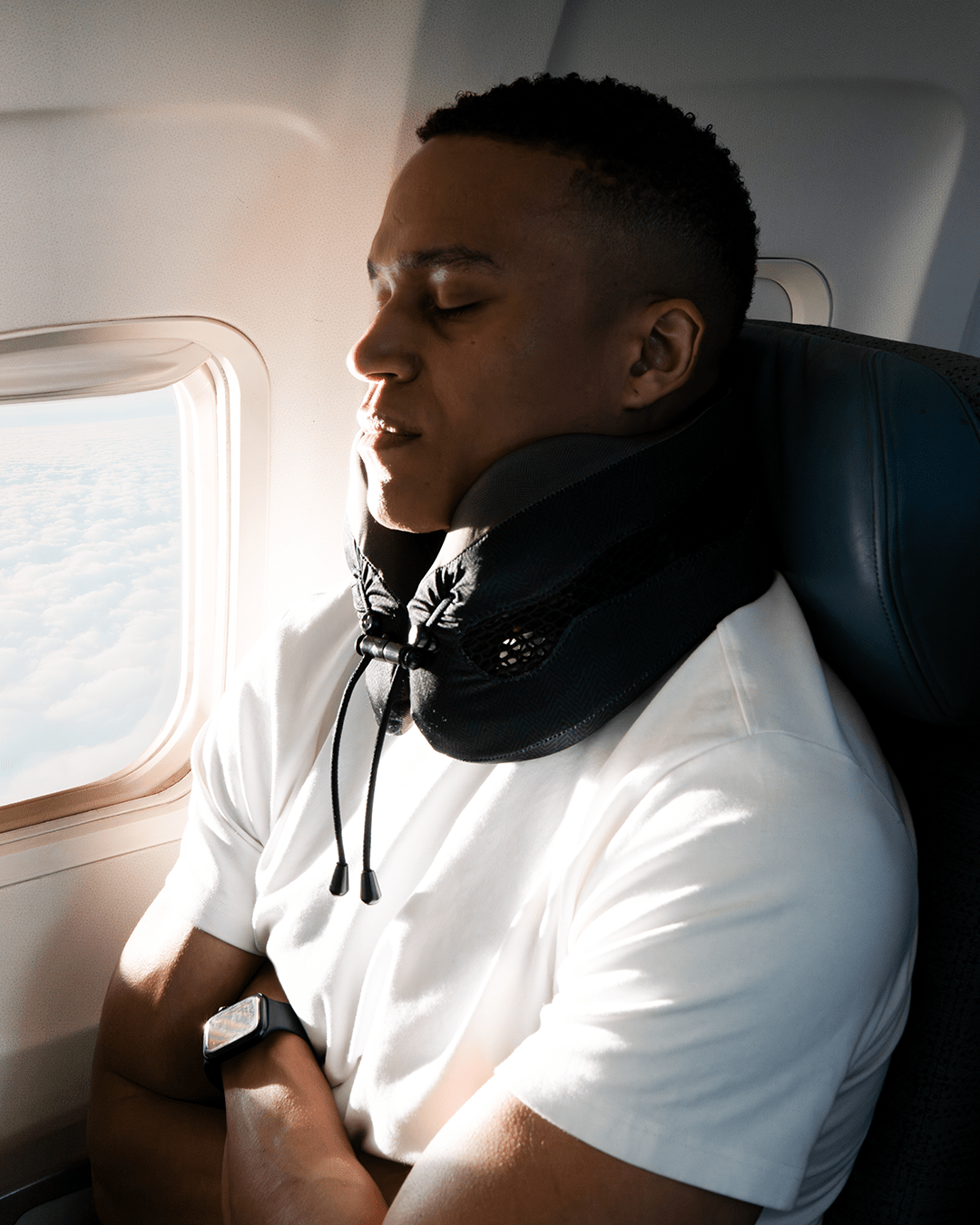 Man sitting in an airplane seat with a neck pillow, looking out the window.