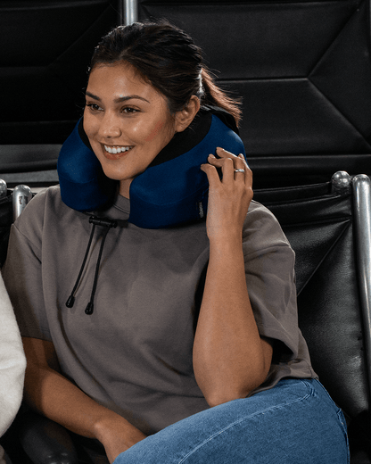 Woman sitting in an airplane terminal seat with a blue Evolution S3 neck pillow on